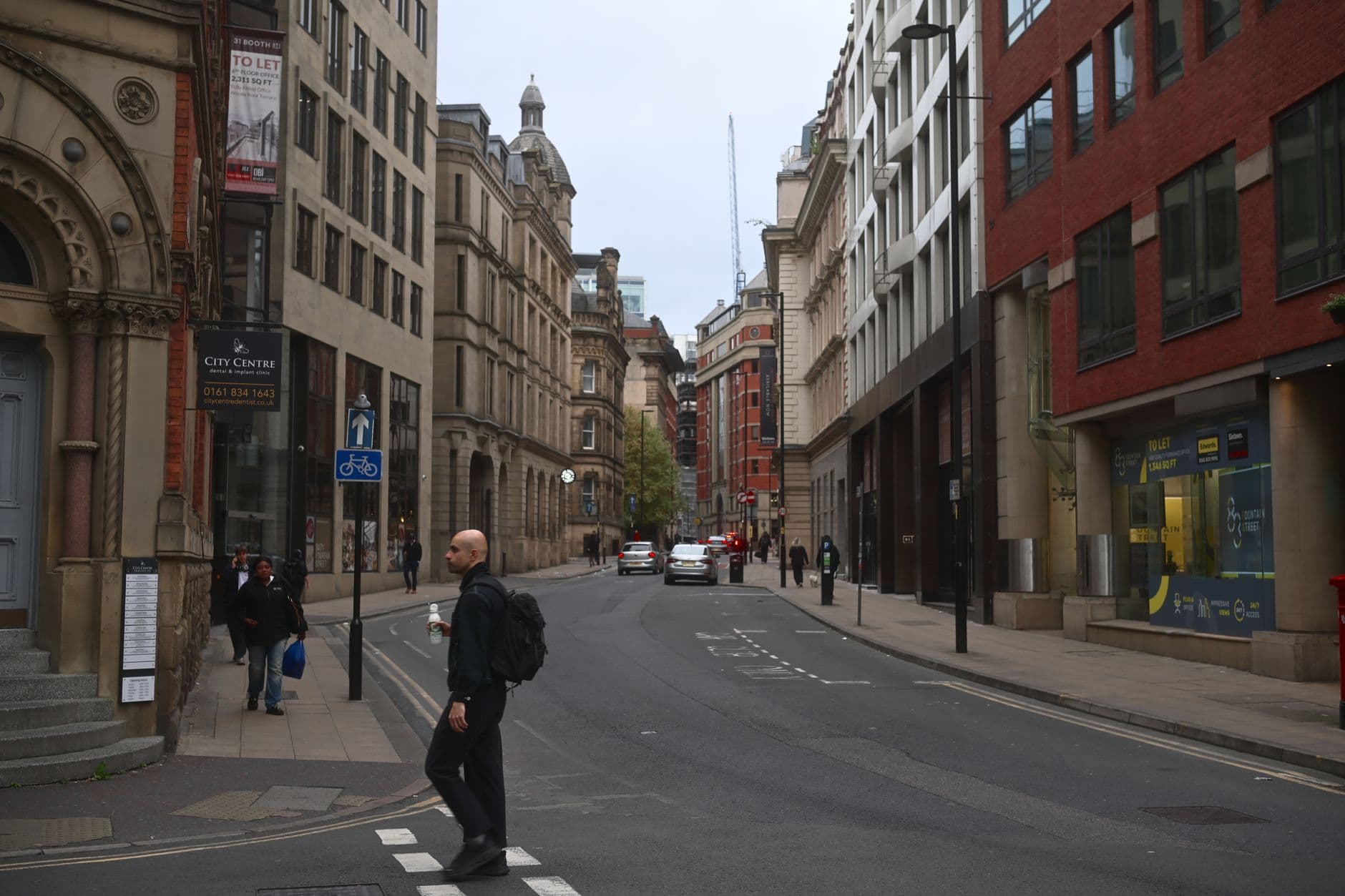 A man crossing the street in Manchester's city centre, with historic architecture.